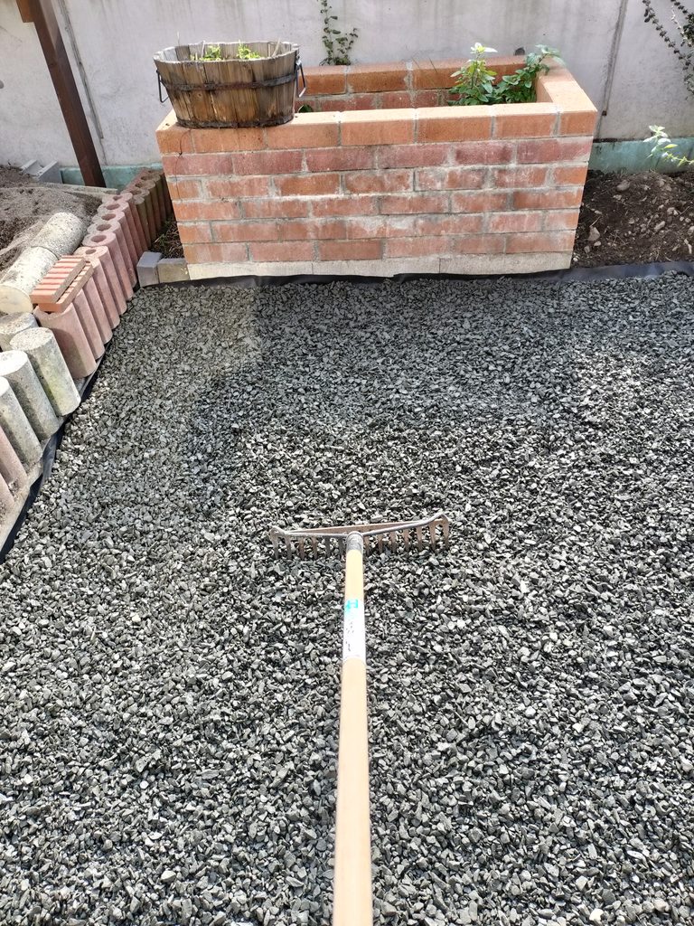 防草シートの上に敷いた砕石をレーキでならす作業